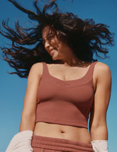 model in a brown ribbed v-neck cropped tank top with flowing hair against a clear blue sky.
