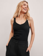 black ribbed tank top with a soft V neckline front and back, overlapping front neckline detail, and a performance lining shelf bra. Tank hits at a high hip length.