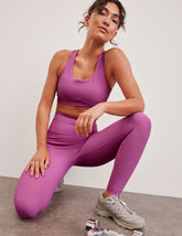 pink medium support racerback bra with a scoop neckline, overlapping hemband detail, is lined with performance lining and powermesh in between, and has removable bra pads.