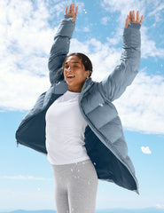 woman wearing a blue puffer coat standing against a mountainous landscape with a clear sky.