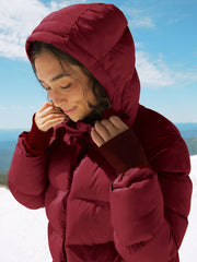 woman wearing a red mid thigh length puffer jacket with a hood against a snowy background.