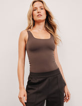 model wearing a brown square neck tank bodysuit and brown pants against a plain background.