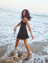 model is wearing a black square neck tank mini dress with pockets.