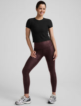 model wearing a black t-shirt and faux leather maroon leggings on a light gray background.