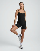 woman wearing a black biker bodysuit and sneakers on a plain background.