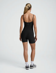 woman wearing a black biker bodysuit and sneakers on a plain background.