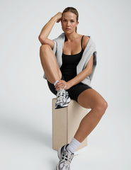 woman wearing a black biker bodysuit and sneakers on a plain background.