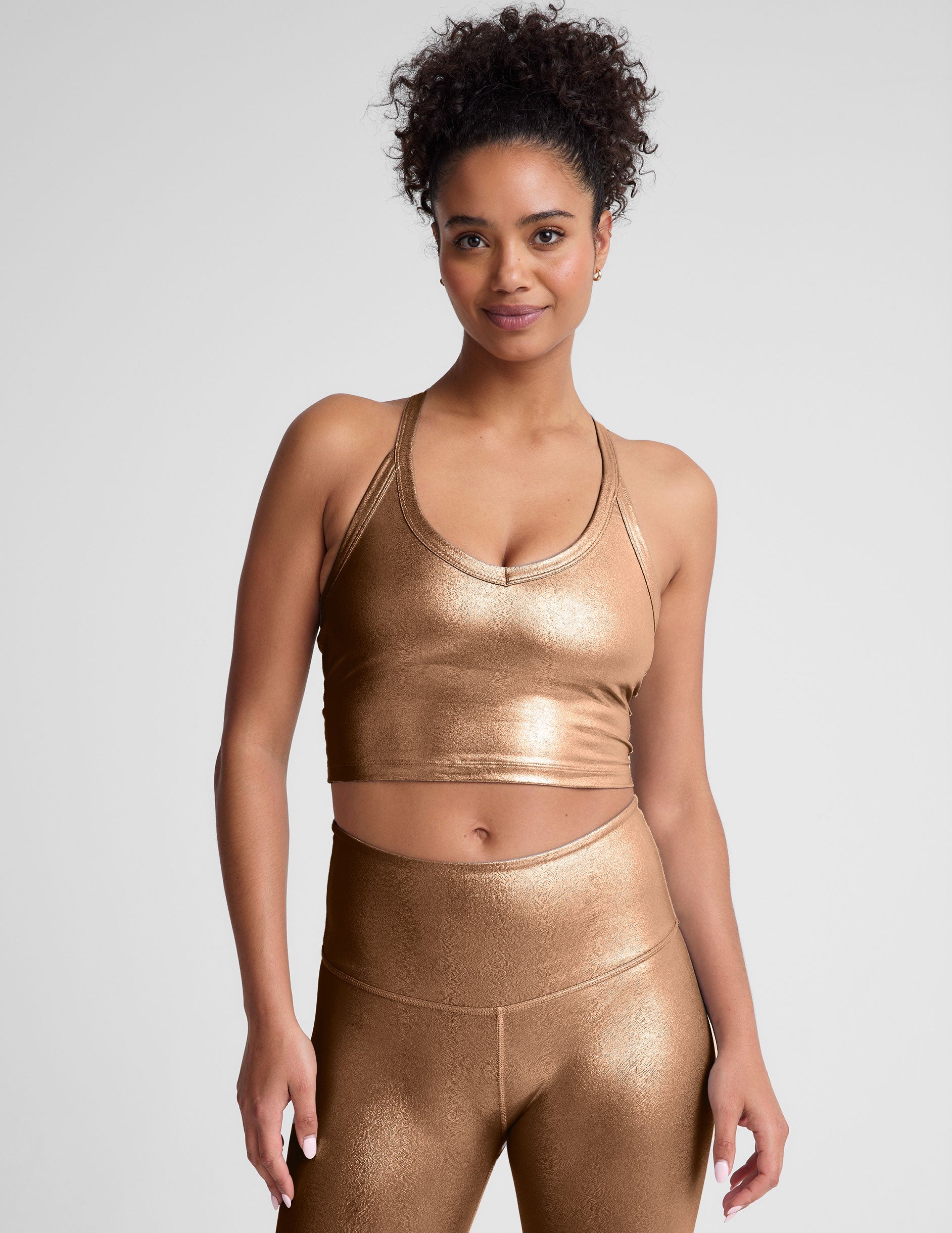 woman wearing a gold v-neck cropped tank and leggings on a plain background.