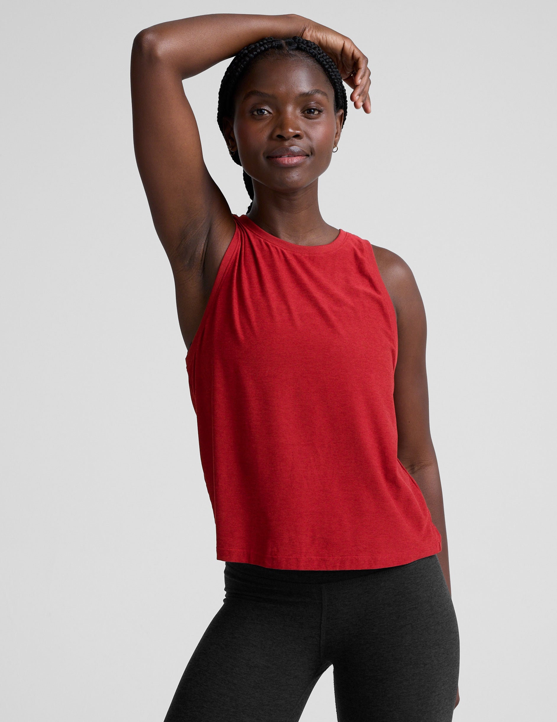 model wearing a red scoop neck sleeveless top and black leggings against a plain background.