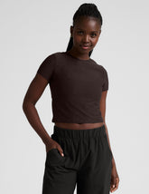 model wearing a brown crop top and black pants against a plain background.