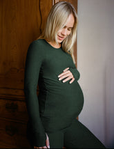model wearing a green long-sleeve maternity top and leggings against a plain background.