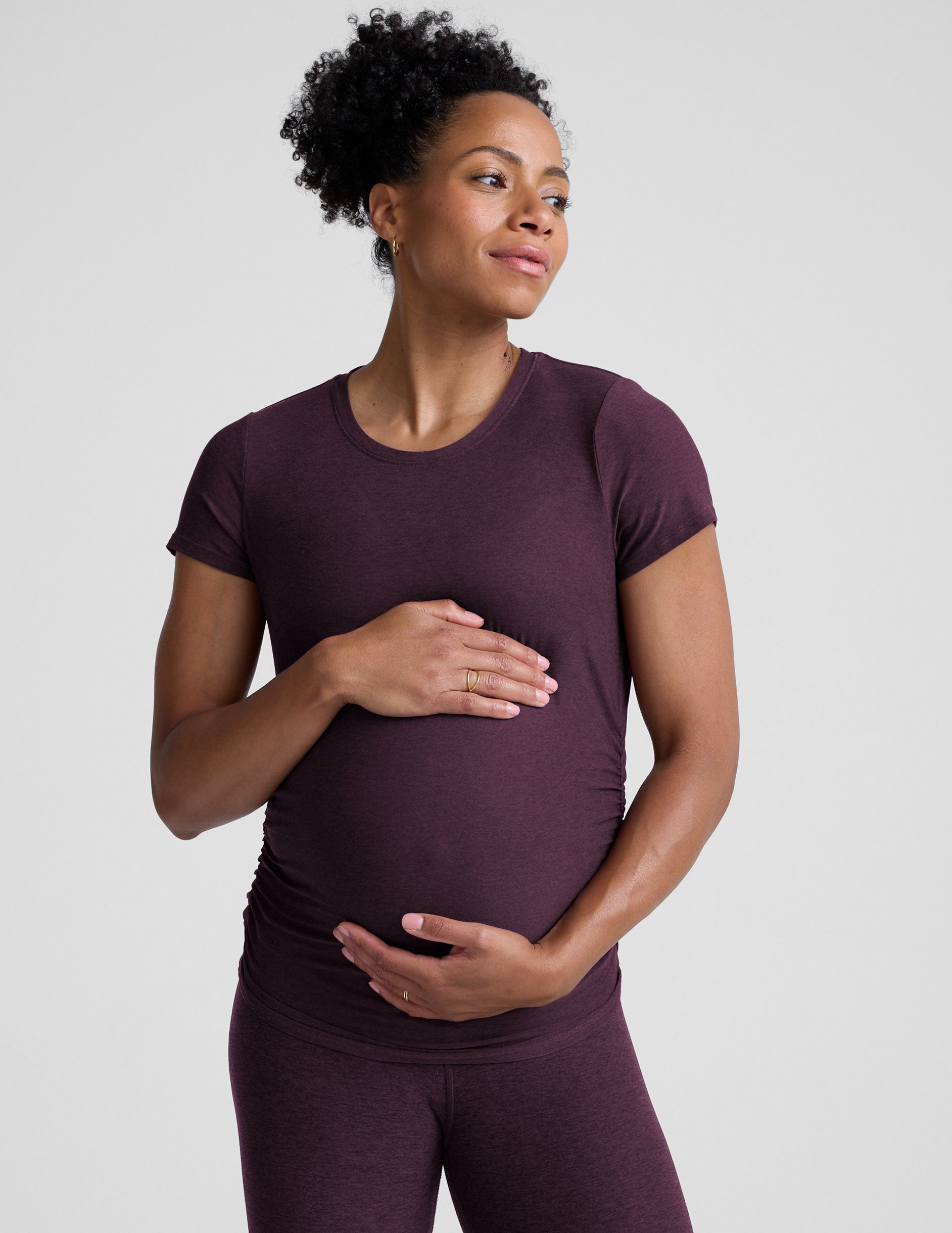 model wearing a purple maternity t-shirt and leggings against a light gray background.