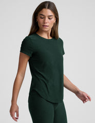 woman wearing a dark green t-shirt and leggings against a plain background.