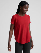 woman wearing a red t-shirt and dark pants on a light gray background.