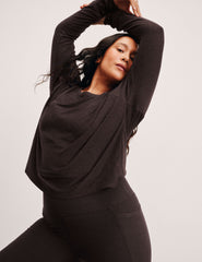 woman wearing a brown long-sleeve top and leggings on a plain background.