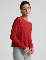 model is wearing a red crewneck long sleeve top and grey leggings against a plain background.