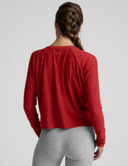 model is wearing a red crewneck long sleeve top and grey leggings against a plain background.
