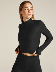 Woman wearing a black long-sleeve top and leggings on a beige background