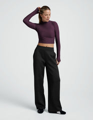 woman wearing a cropped purple long-sleeve mock-neck top and black pants on a plain background.