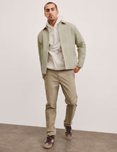 man wearing a light jacket and beige chino pants against a plain background.