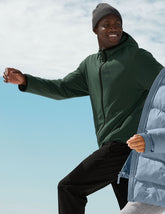 man wearing a green jacket and black pants against a blue sky.