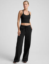 woman wearing a black cropped tank and fleece pinktuck pants on a plain background.