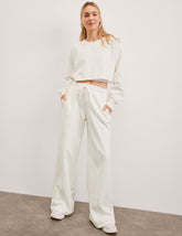 model wearing a white crew neck sweatshirt and white fleece wide leg pants against a plain background.