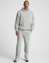 man wearing a gray hoodie and straight leg fleece sweatpants on a plain background.