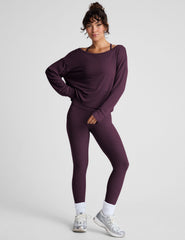 model wearing a dark purple long-sleeve boat neck sweater and leggings on a light gray background.