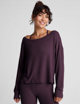 model wearing a dark purple long-sleeve boat neck sweater and leggings on a light gray background.