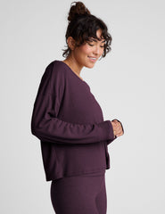 model wearing a dark purple long-sleeve boat neck sweater and leggings on a light gray background.