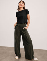 model wearing a black top and green wide-leg pants against a plain background.