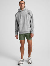 man wearing a gray hoodie and green shorts on a white background.