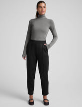 woman wearing a gray turtleneck and black tapered pants on a white background.