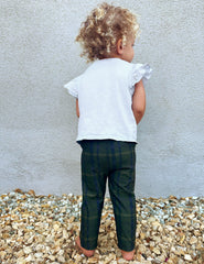 model wearing a white top and green plaid pants standing on gravel against a light gray wall.