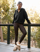 model wearing a black quarter zip pullover and leopard printed midi length leggings on a porch with blurred trees in the background.