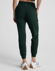 person wearing dark green jogger pants and white sneakers on a plain background.