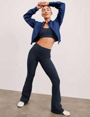 woman wearing a blue jacket and dark pants on a plain background.