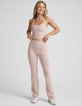 model wearing a pink cropped racerback tank top and pink high-waisted bootcut pants with pockets set on a plain background.