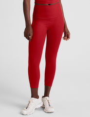 woman wearing a red cropped tank and capri length leggings on a plain background.