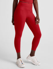 woman wearing a red cropped tank and capri length leggings on a plain background.