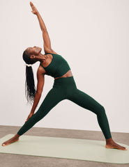person in green slim racerback cropped tank and leggings performing a yoga pose on a mat.