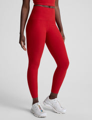 woman wearing a red slim racerback cropped tank top and high-waisted midi length leggings against a plain background.