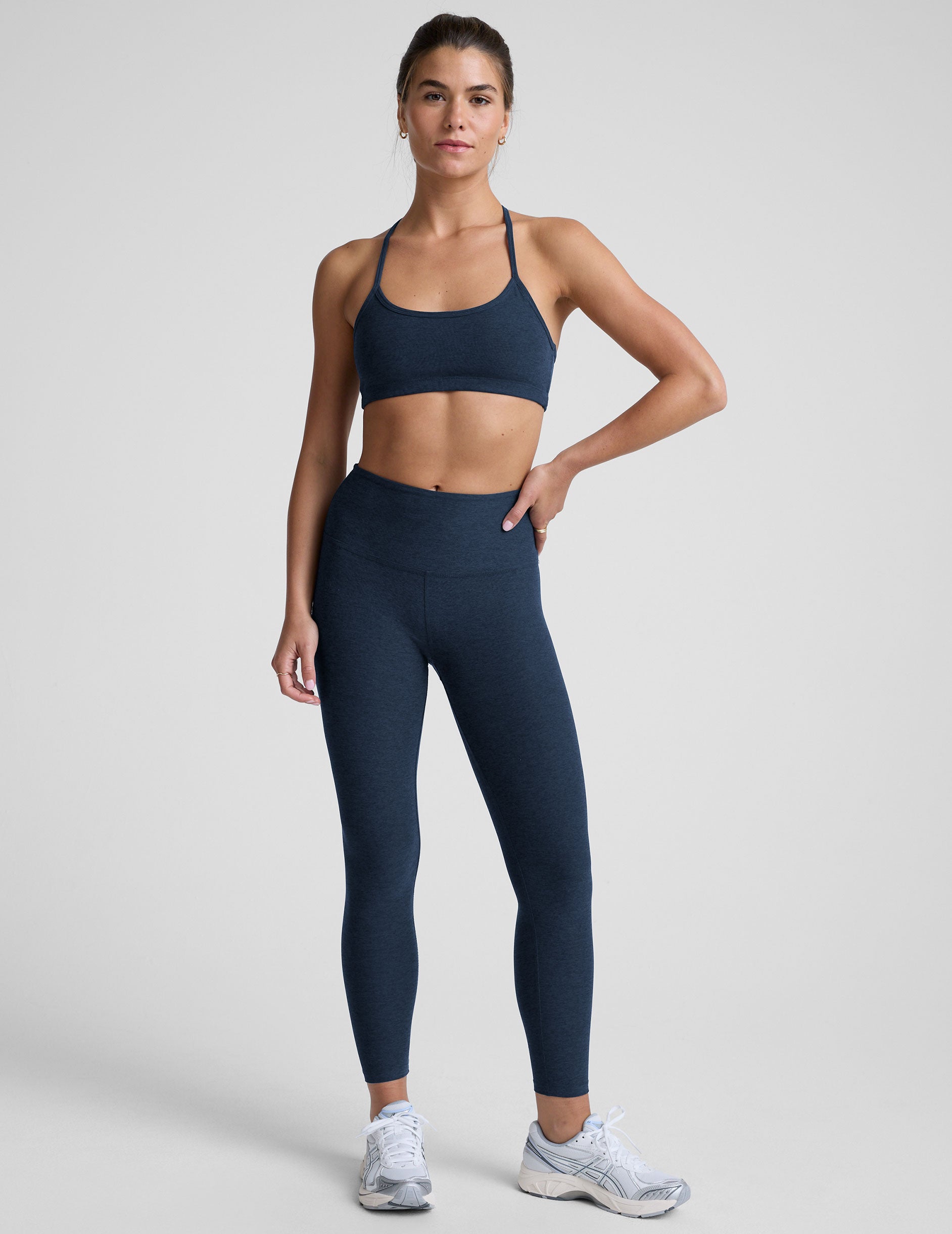 model is wearing a navy blue racerback sports bra and navy blue leggings on a light gray background.