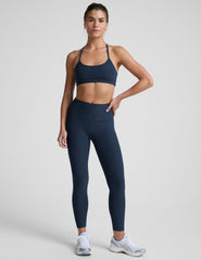 model is wearing a navy blue racerback sports bra and navy blue leggings on a light gray background.
