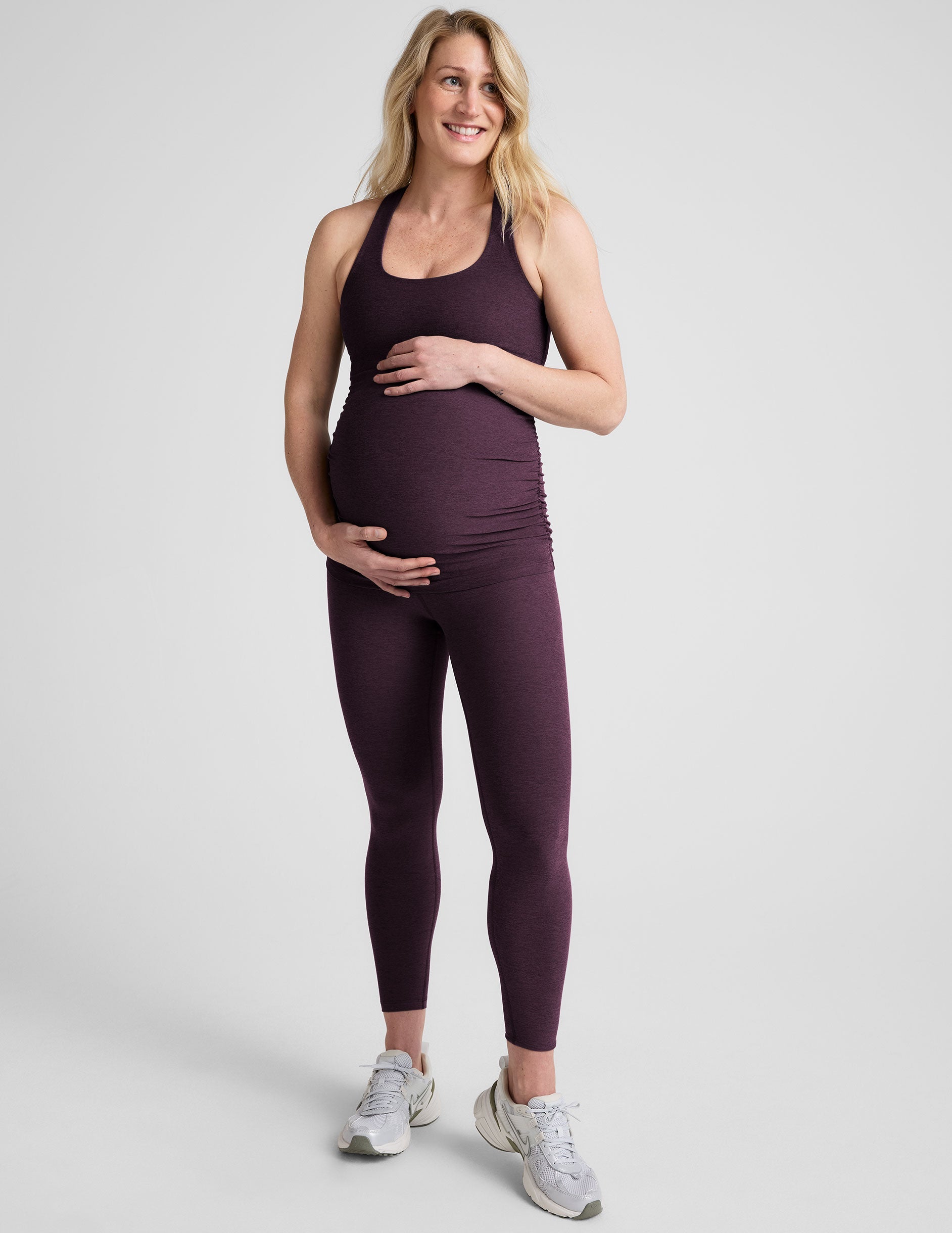 model wearing a purple maternity racerback tank and purple maternity midi length leggings on a plain background.