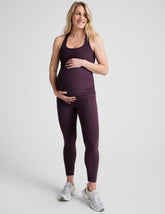 model wearing a purple maternity racerback tank and purple maternity midi length leggings on a plain background.