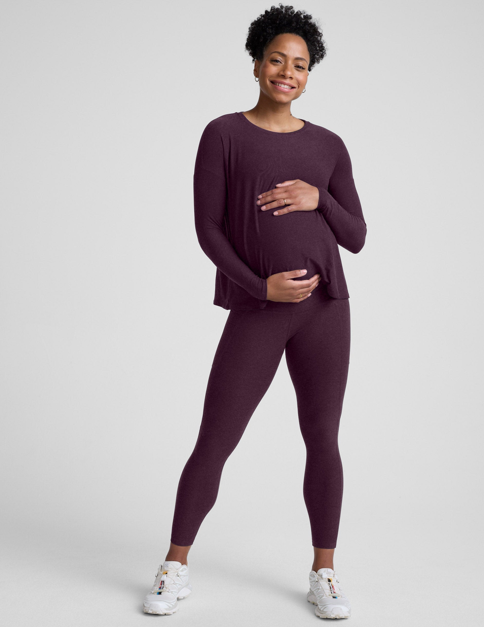 pregnant woman wearing a long sleeve maternity top and leggings with pockets against a plain background.