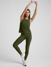 woman in an army green tank and legging stretching on a light gray background.