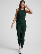 model is wearing a green tank top and green high-waisted midi length leggings with pockets on a plain background.